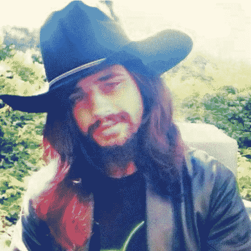 Michael letting a soft smile radiate off his face. The sun behind him gives him an angelic light, and his black cowboy hat and long wavy hair frame his face in diffused sunlight.