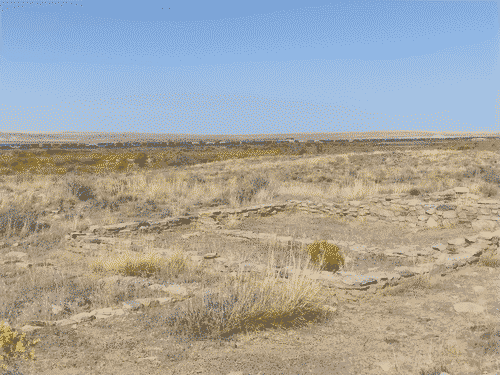 Looking north from Puerco Pueblo Ruins, past an ancient building foundation, over the fields, toward a huge freight train in the distance