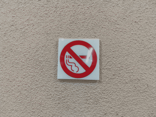 A wordless no smoking sign installed upside down on a stucco column