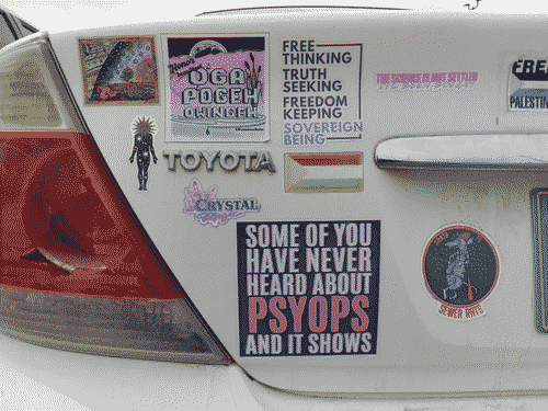 Left half of the backside of a white late-2000s Toyota camry, with various stickers. The most prominent reads: some of you have never heard about psyops and it shows. Others show support for Palestine; the science is not settled, it