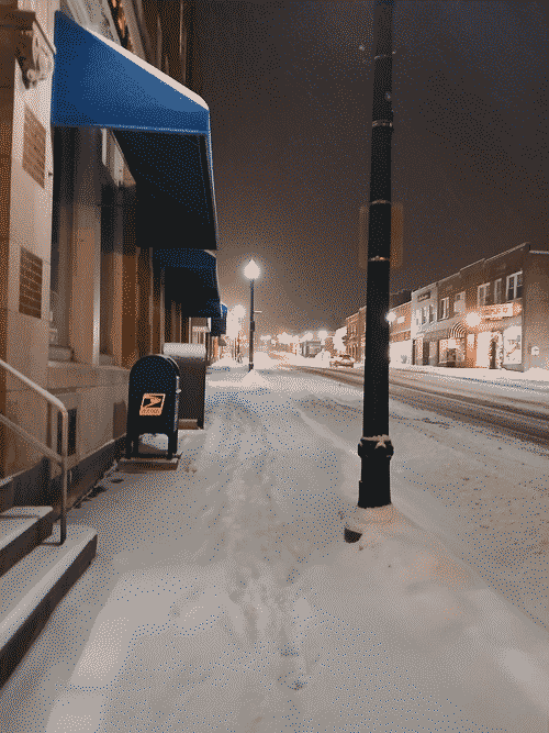 Main street in Ellsworth after a heavy snow. The ground is pure white and the light pollution glows on the horizon amidst the crowded brick buildings